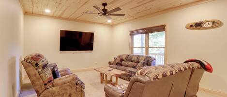 Una sala de estar con ventilador de techo, un televisor de pantalla plana grande, un sofá, una silla y una mesa de centro.