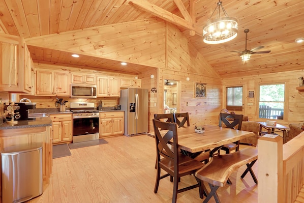 A spacious wooden cabin with a kitchen featuring stainless steel appliances, a dining area with wooden tables and chairs, and a ceiling fan. - Hot Tub & Fire Pit: Secluded Blue Ridge Cabin! (Blue Ridge)