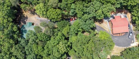 An aerial view of a property with dense forestation, a red-roofed building, and a paved driveway.