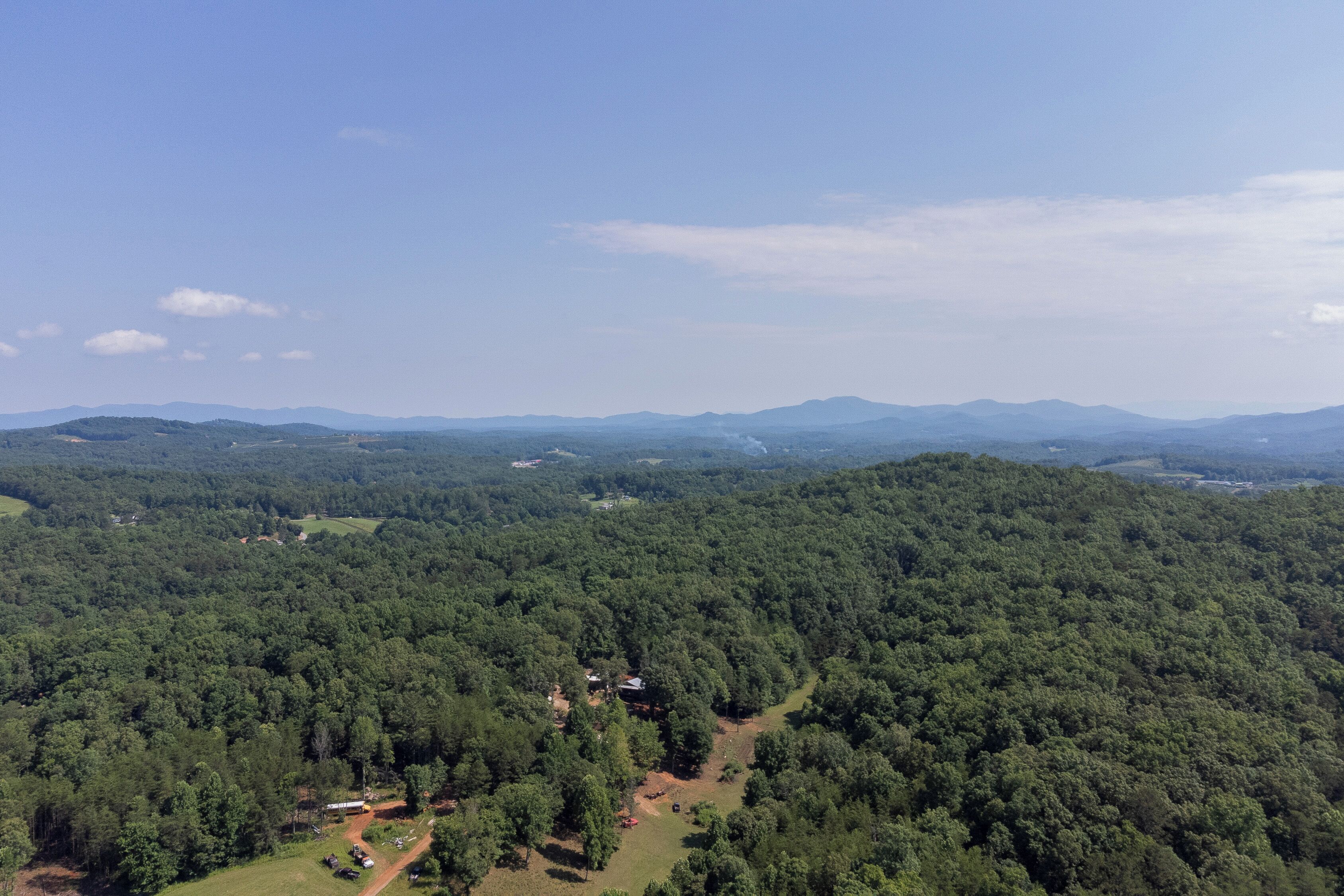 An aerial view of a forested area with a small building surrounded by trees and a clear sky.