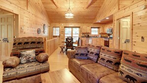 Ein Holzblockhaus-Interieur mit Sofa, Sesseln, Essbereich und Küche.
