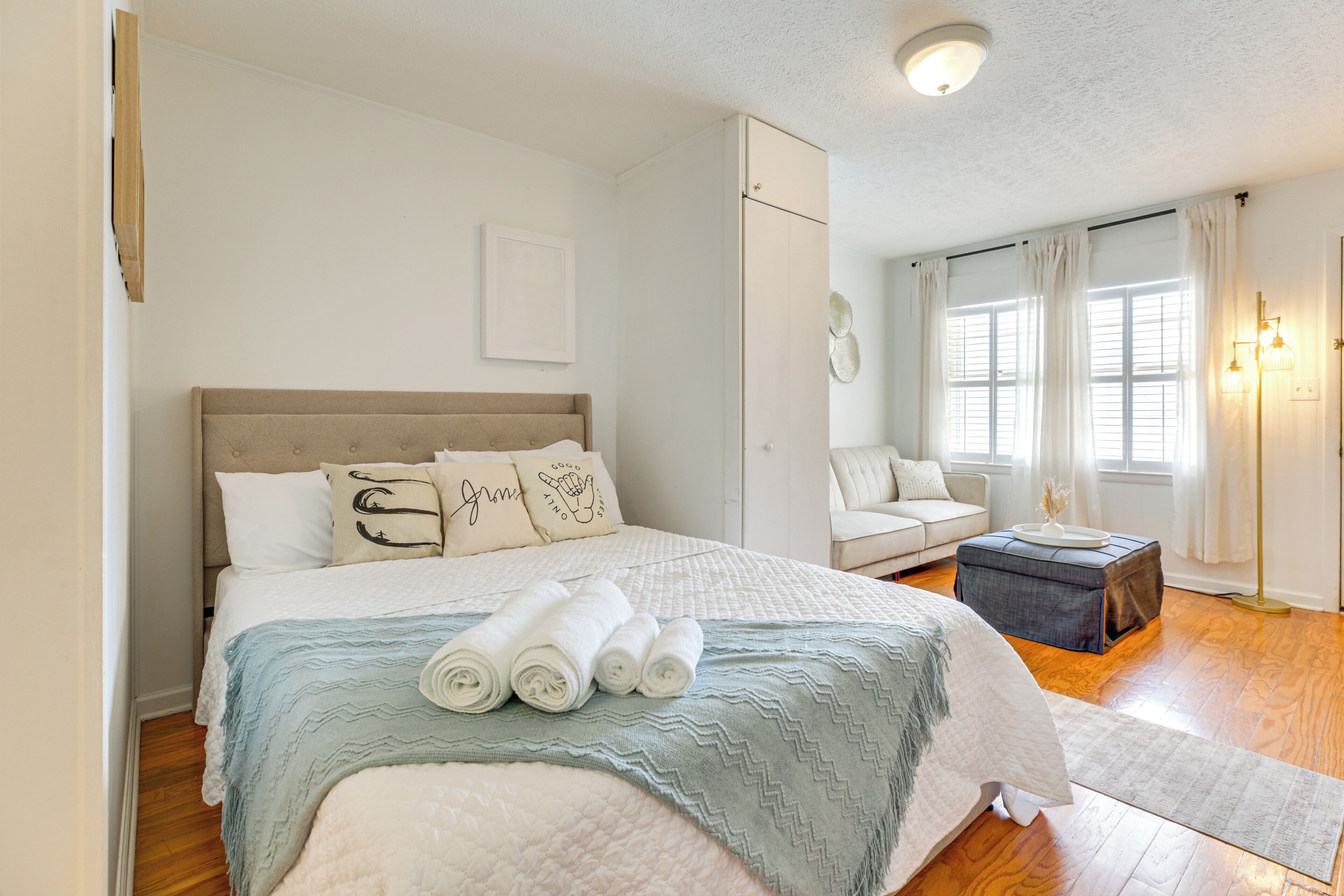 A bedroom with a large bed, a bedside table, a chair, and a window with curtains.