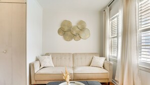 A living room with a beige sofa, a round coffee table with a vase, and a wall art piece above the sofa. - Walk to North Myrtle Beach: Studio w/ Pool Access! (North Myrtle Beach)