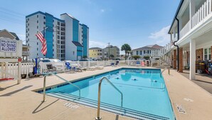 A swimming pool with a shallow water sign, surrounded by buildings and a white picket fence. - Walk to North Myrtle Beach: Studio w/ Pool Access! (North Myrtle Beach)