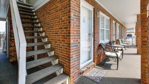 A brick building with a staircase leading to a door, a covered outdoor seating area with chairs and tables, and a window with a view. - Walk to North Myrtle Beach: Studio w/ Pool Access! (North Myrtle Beach)
