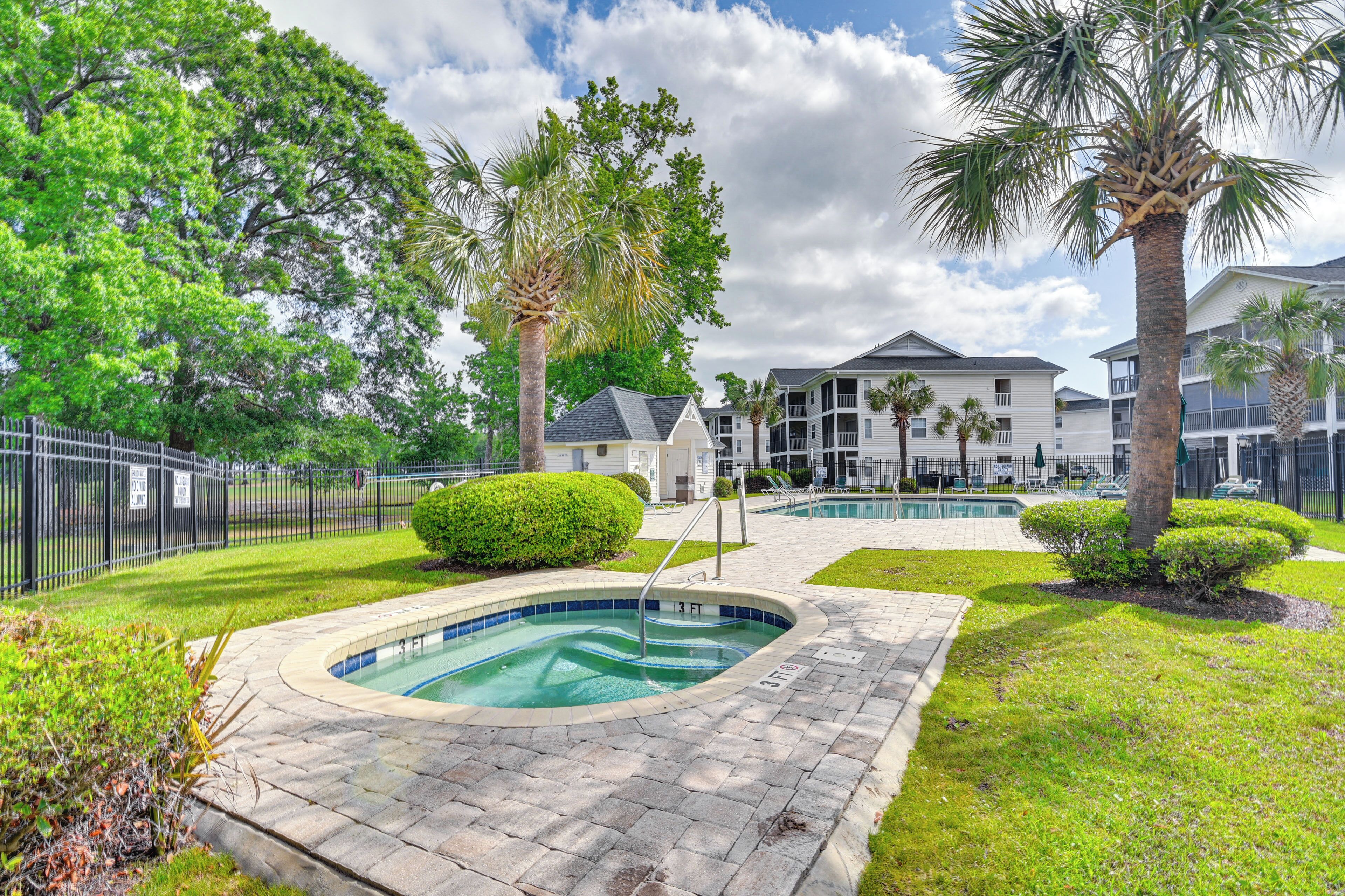 A swimming pool area with a paved deck, surrounded by well-maintained grass and palm trees.