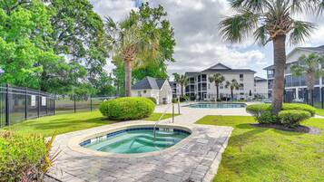 A swimming pool area with a paved deck, surrounded by well-maintained grass and palm trees.