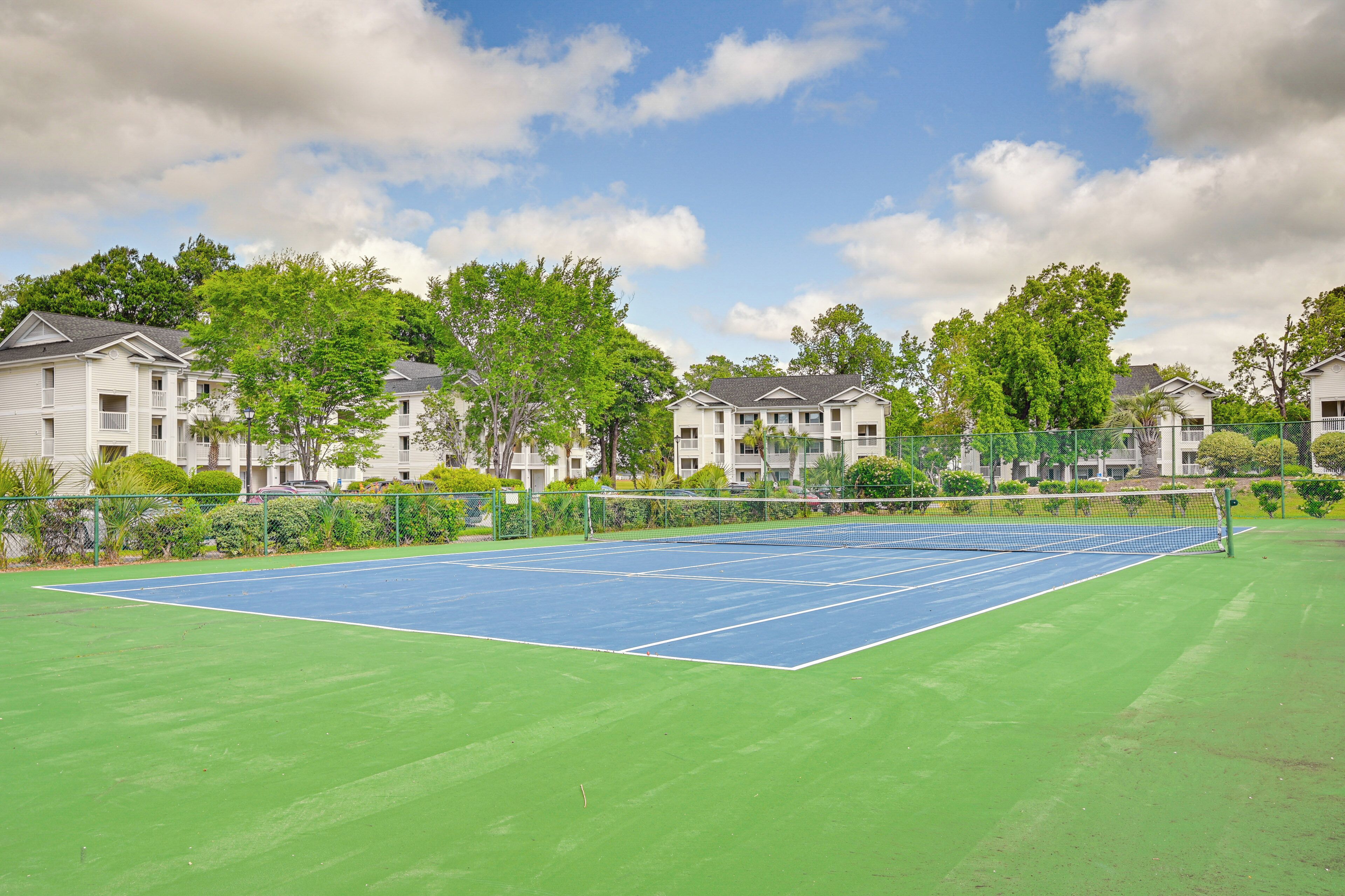 Un court de tennis avec un filet, entouré de verdure et d’immeubles d’habitation.