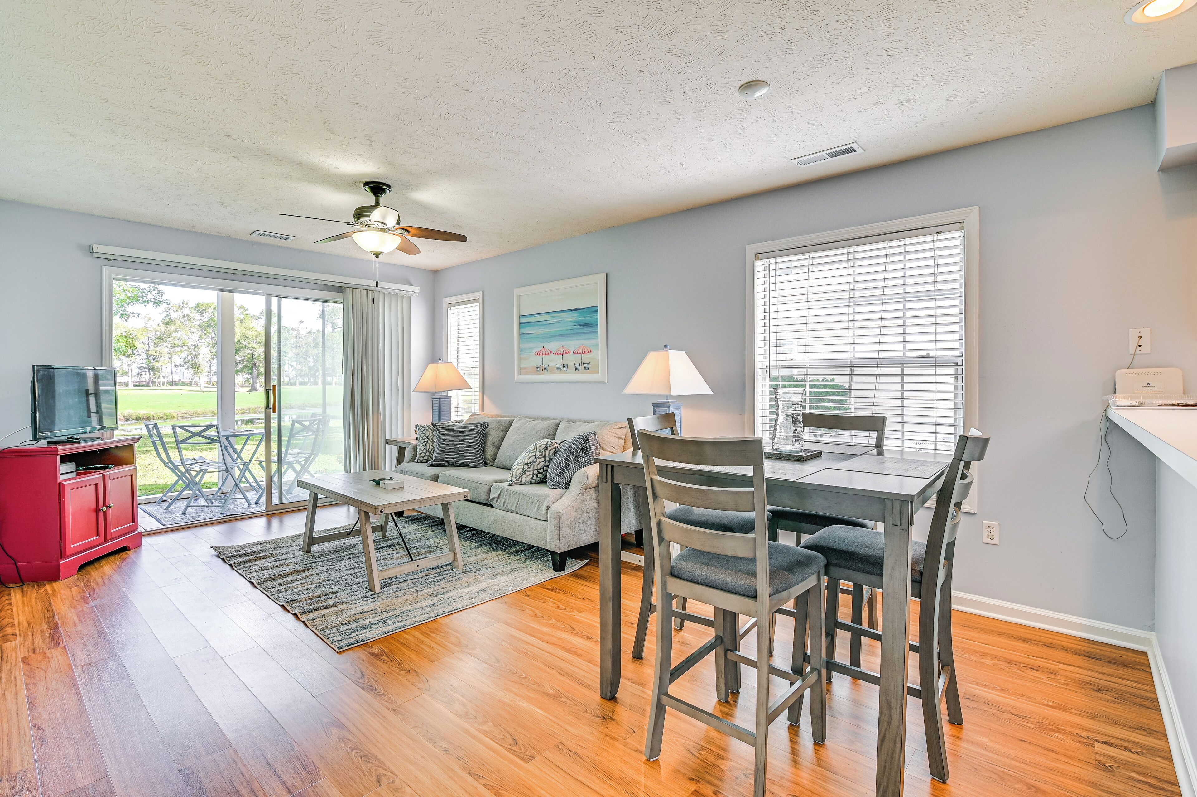 A spacious living room with a sofa, a dining table with chairs, a ceiling fan, and a TV on a red cabinet.