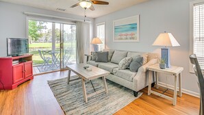 A living room with a sofa, coffee table, TV stand, and a ceiling fan. - Myrtle Beach Condo w/ Pool Access: 5 Mi to Ocean (Myrtle Beach)