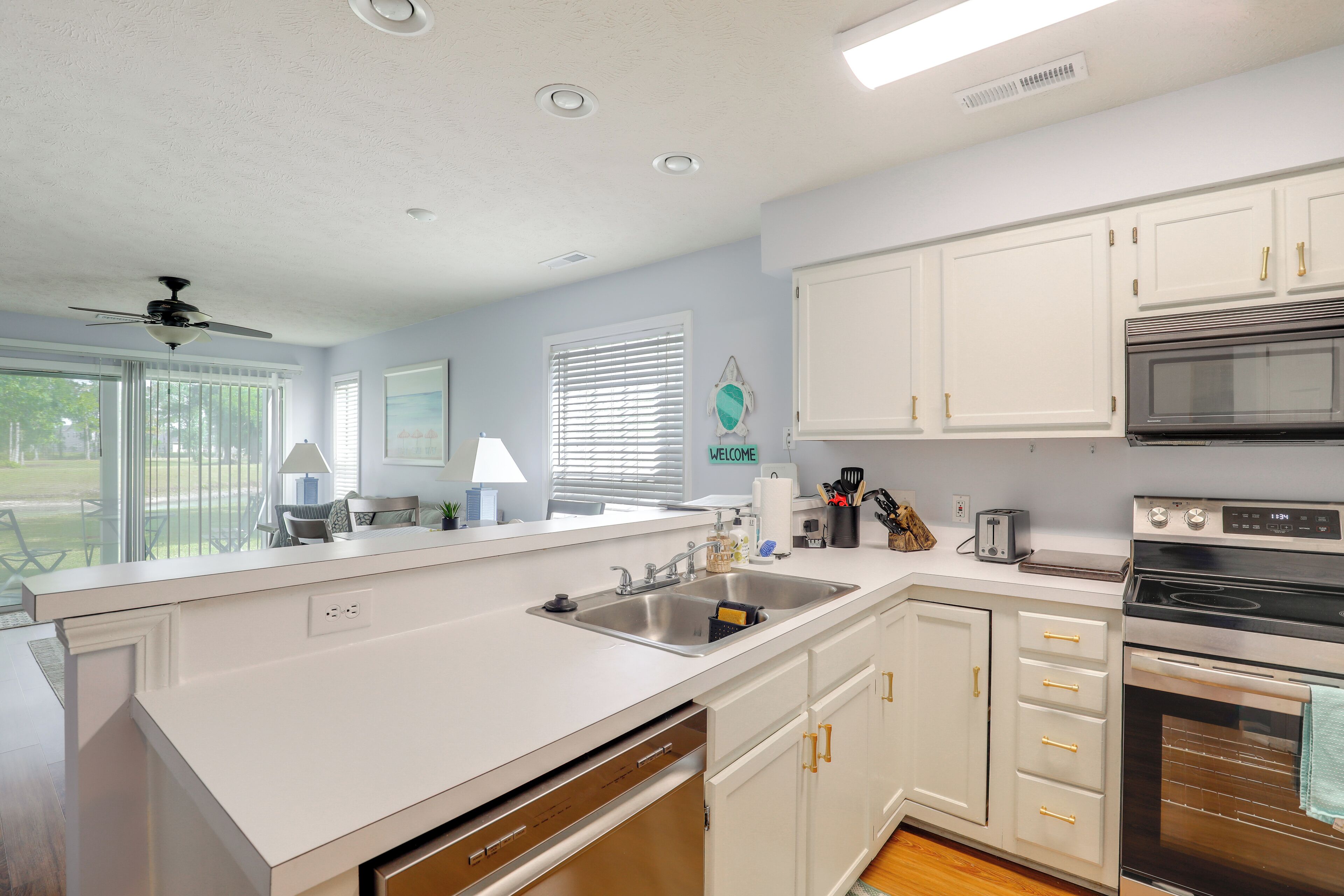 A kitchen with white cabinets, a stainless steel sink, a microwave, and an oven.