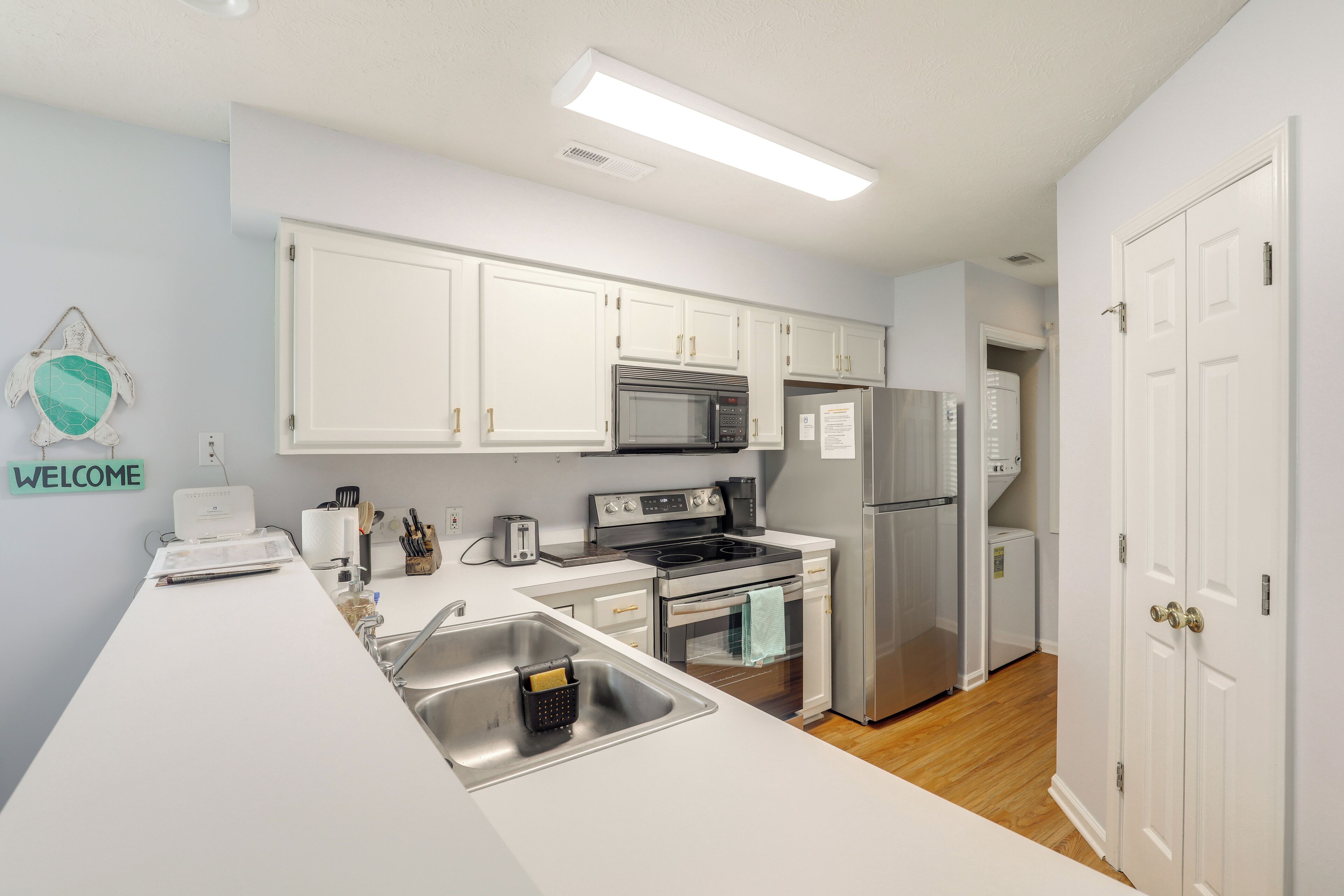 A modern kitchen with white cabinets, stainless steel appliances, and a 'WELCOME' sign on the wall.