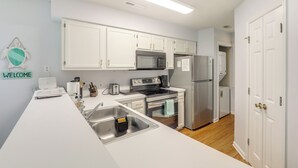 A modern kitchen with white cabinets, stainless steel appliances, and a 'WELCOME' sign on the wall. - Myrtle Beach Condo w/ Pool Access: 5 Mi to Ocean (Myrtle Beach)