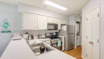 A modern kitchen with white cabinets, stainless steel appliances, and a 'WELCOME' sign on the wall.
