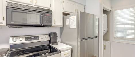 A kitchen with white cabinets, a stainless steel refrigerator, a microwave, and a stove.