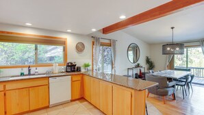 A modern kitchen with wooden cabinets, a granite countertop, and a dining area with a table and chairs. - Ping-pong & Private Hot Tub: Family Cabin in Bend! (Bend)