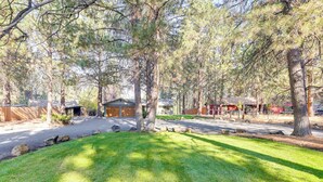 A residential area with a well-maintained lawn, several trees, and a small building with a sloped roof. - Ping-pong & Private Hot Tub: Family Cabin in Bend! (Bend)