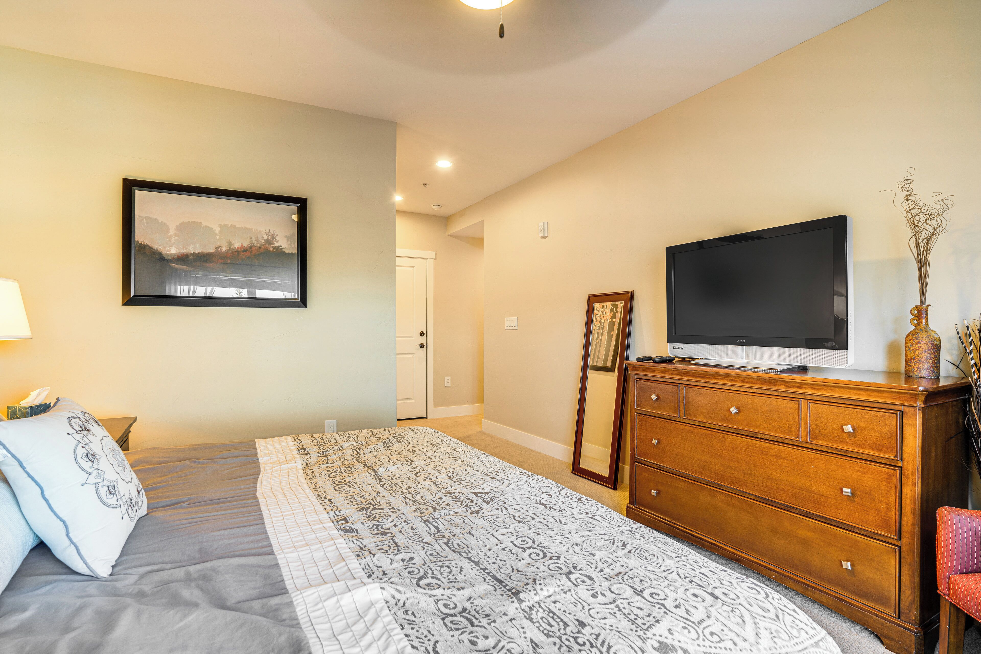 Ein Schlafzimmer mit Bett, Kommode, Fernseher und einem gerahmten Bild an der Wand.