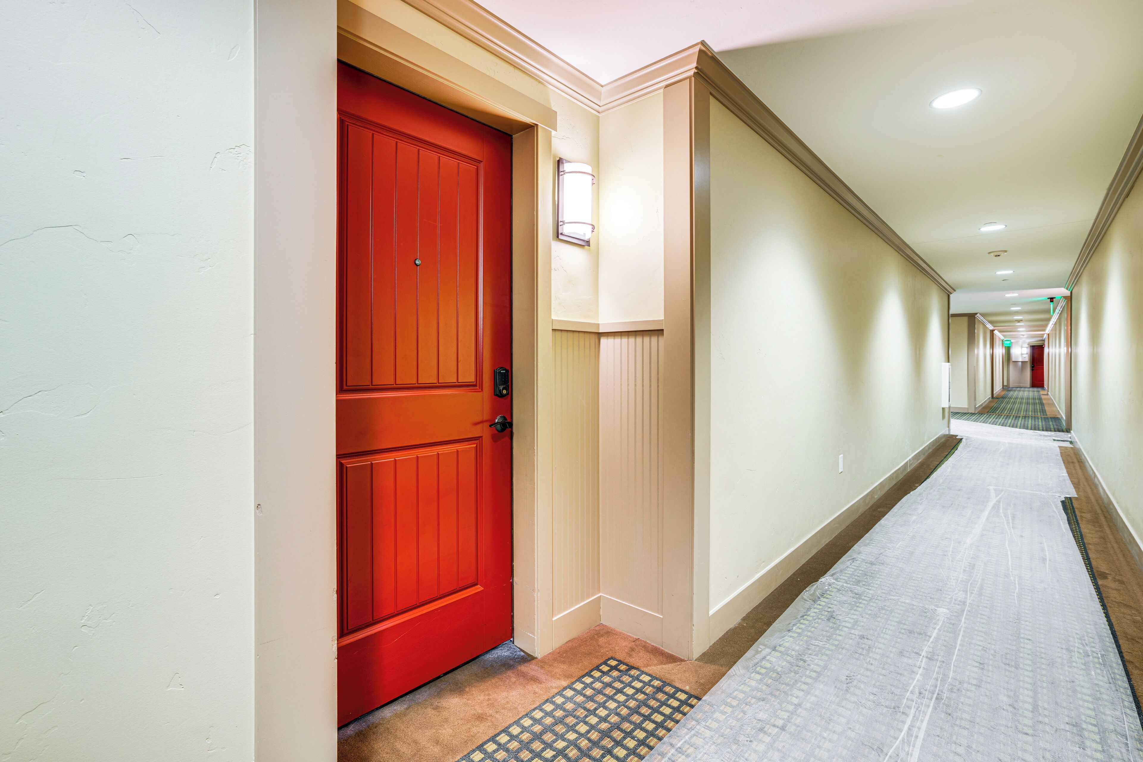 A hotel hallway with a red door, beige walls, and a carpeted floor.