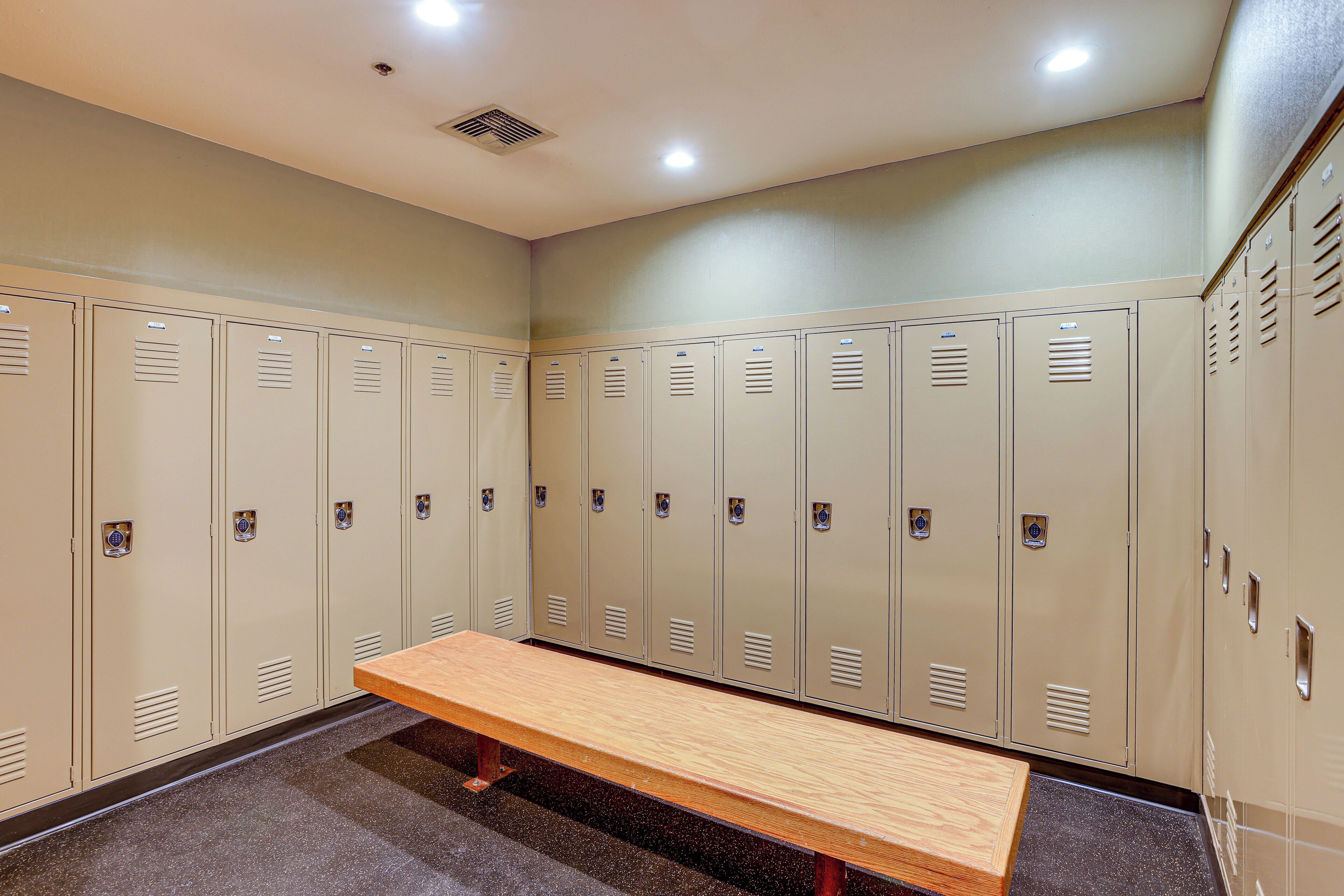 A locker room with beige lockers, a wooden bench, and a tiled floor.