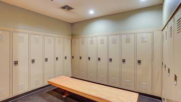 A locker room with beige lockers, a wooden bench, and a tiled floor.
