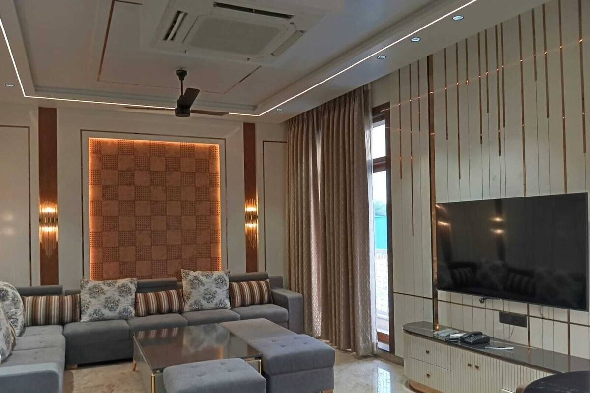 A modern living room with a sectional sofa, ottomans, a coffee table, a flat-screen TV, and a decorative wall panel.