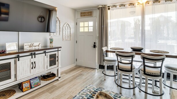 A dining area with a white door, a sign reading "We are blessed," and a view of buildings through sheer curtains. - 2 Blocks to Beach: Modern Condo in North Wildwood! (North Wildwood)
