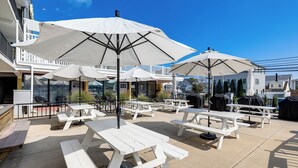 Outdoor picnic tables with white umbrellas, a barbecue grill, and a pool in the background. - 2 Blocks to Beach: Modern Condo in North Wildwood! (North Wildwood)