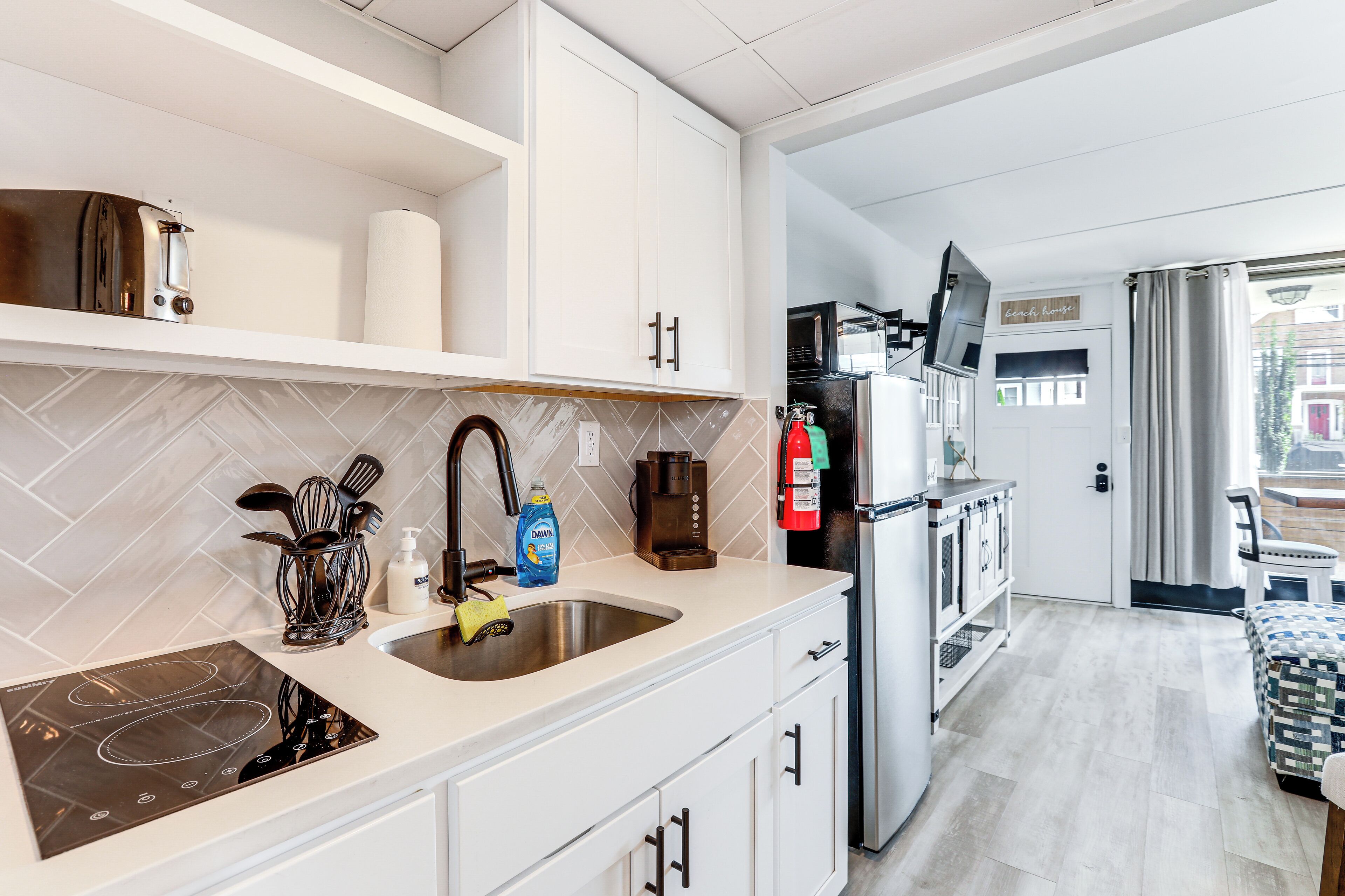 Una cocina moderna con armarios blancos, un lavamanos de acero inoxidable y una placa vitrocerámica integrada.