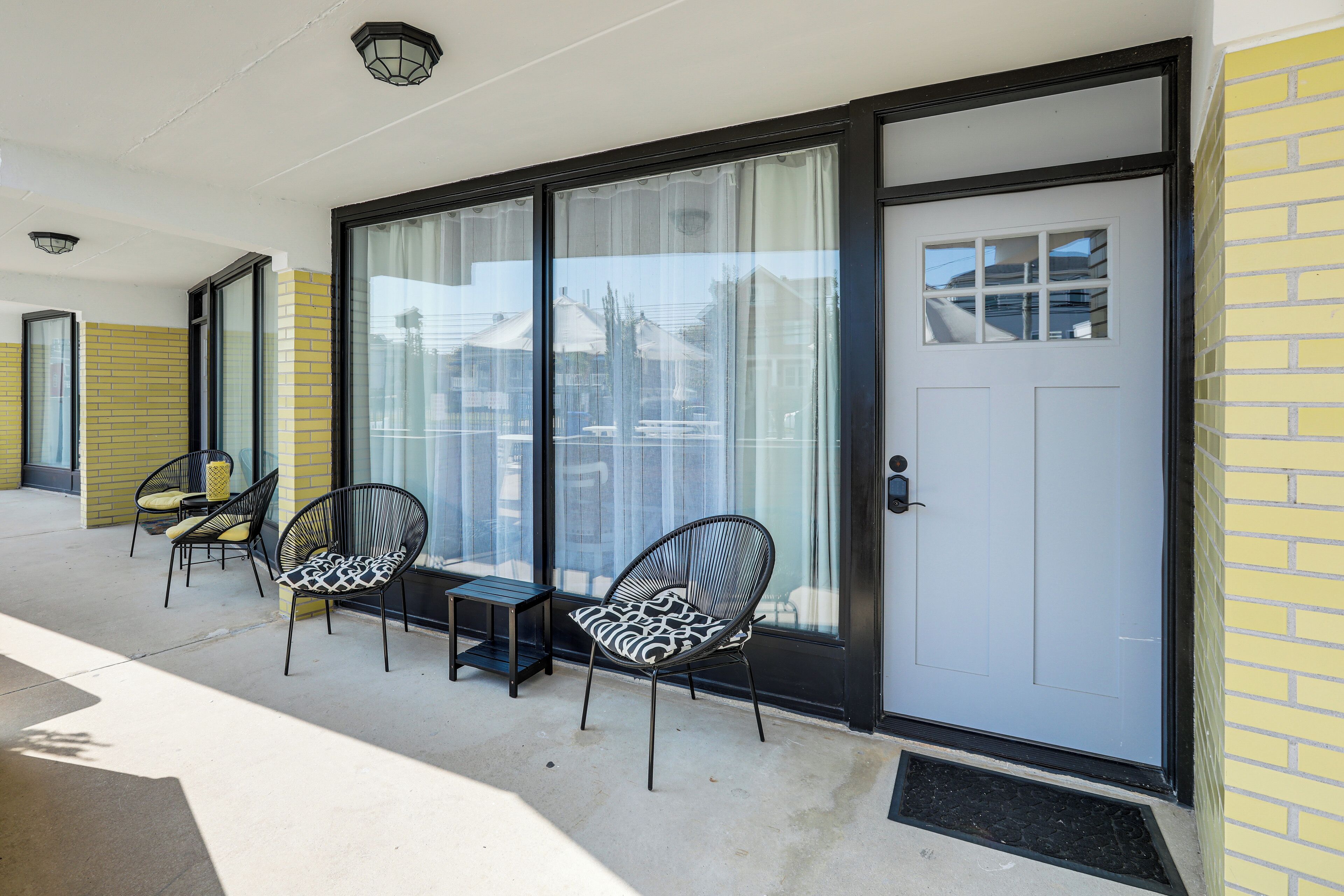A balcony with two chairs and a small table, a sliding glass door, and a yellow brick wall.