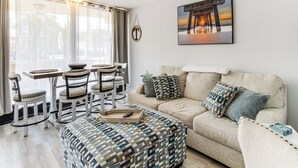 A living room with a sofa, ottoman, and dining set. - 2 Blocks to Beach: Modern Condo in North Wildwood! (North Wildwood)