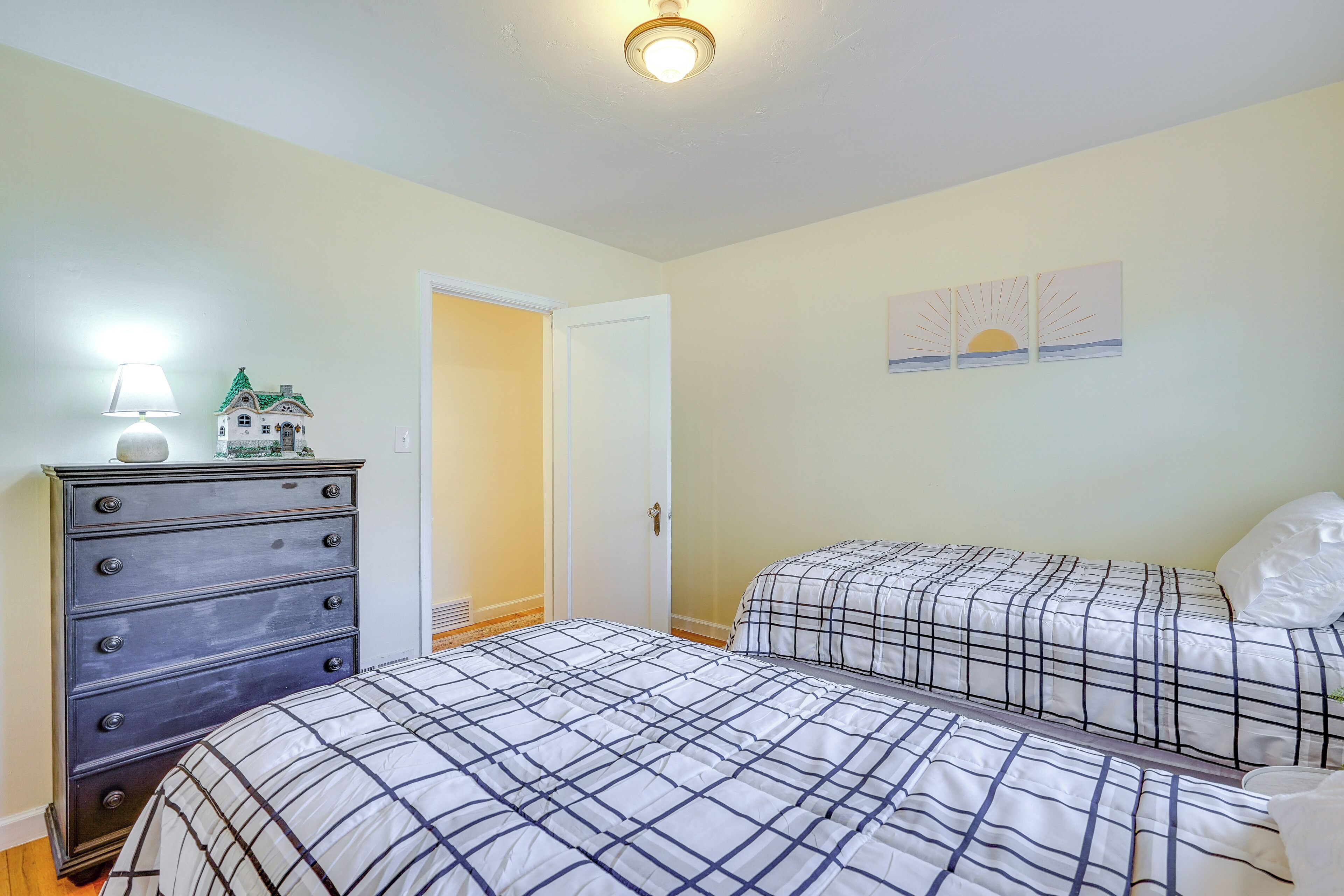Une chambre avec deux lits, une commode et une porte donnant sur une autre pièce.