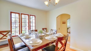 Comedor con una mesa de madera dispuesta para seis personas, sillas alrededor, ventanas amplias y una araña.