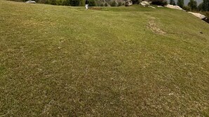 A grassy field with a person standing in the distance, surrounded by mountains and trees. - Vansh Green View Homestay (Sainj)