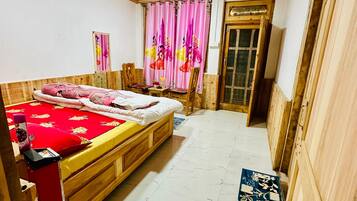 Quarto com teto de madeira, cama com colcha vermelha e branca, piso de madeira e cortinas cor de rosa.
