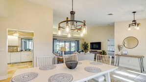 Un vaste espace dédié à la salle à manger, avec une grande table, de nombreuses chaises et un grand vase décoratif au centre. On y trouve également un ventilateur de plafond, un téléviseur et un miroir fixés aux murs.