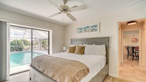 Une chambre dotée d’un grand lit, d’un ventilateur de plafond, d’une vue sur une piscine et d’un coin repas avec une table et des chaises.