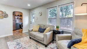 A living room with a beige sofa, a coffee table, and a rug. There is a window with a view of trees and a door leading to a kitchen. - 4 Mi to Dtwn: Cozy Home in Pueblo (Pueblo)