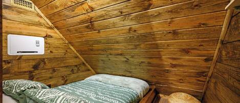 Una habitación de cabaña de madera con una cama, una cesta tejida y un calentador fijado a la pared.