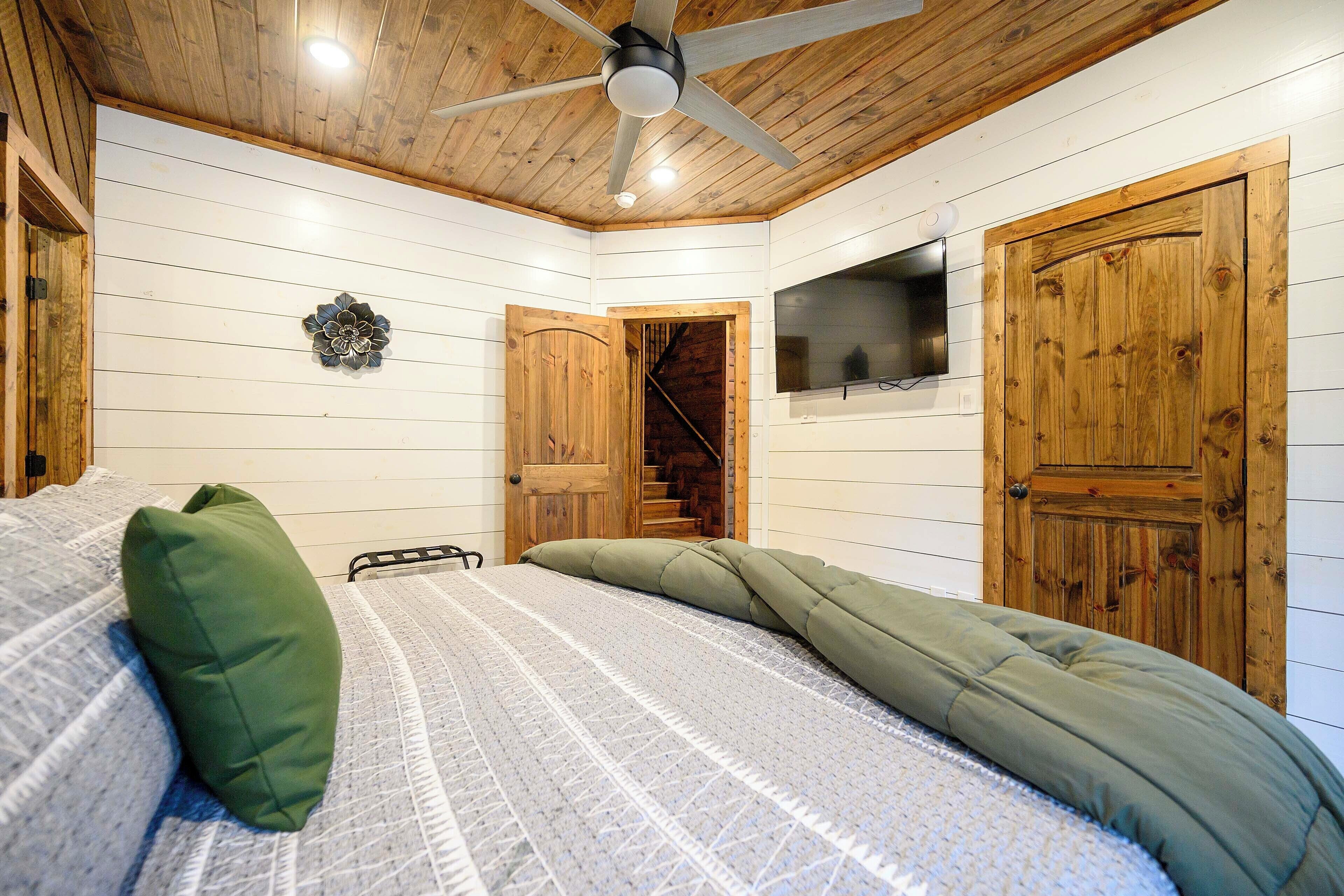A bedroom with a bed, a ceiling fan, wooden walls, a TV, and a staircase.