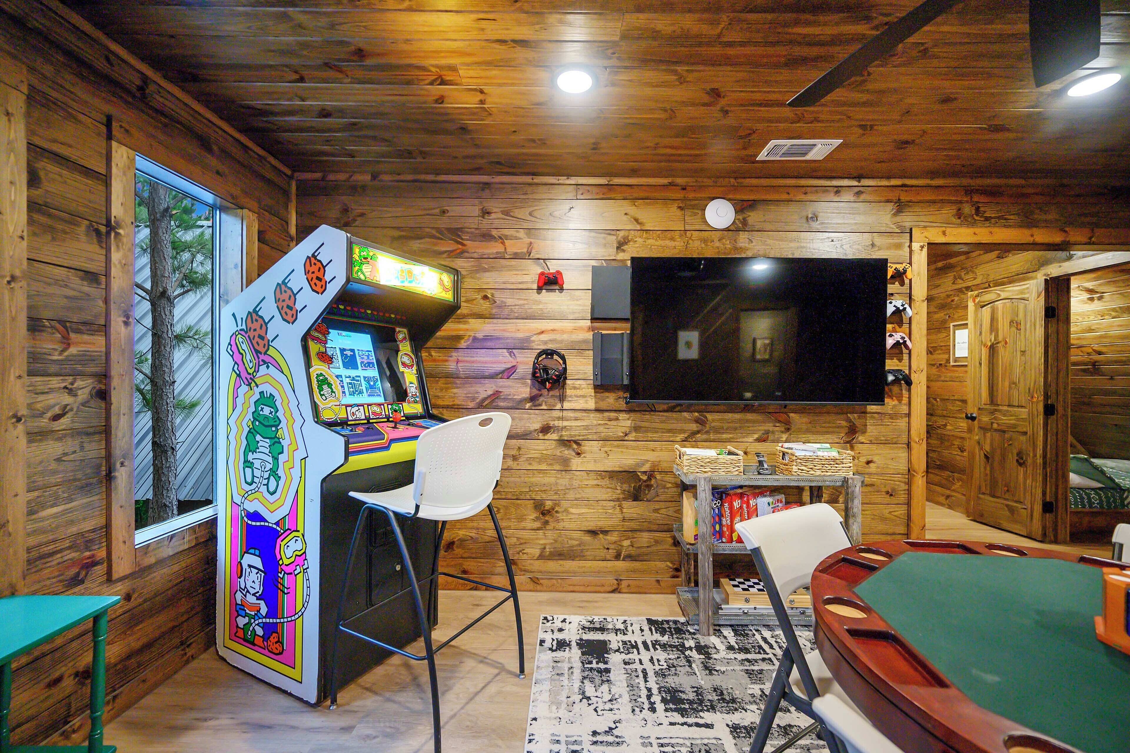 A room with wooden walls, a television mounted on the wall, a pool table, and an arcade machine.