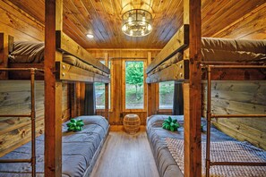 Una cabaña con paredes y suelos de madera, dos literas, una cesta tejida y vistas al verdor a través de una ventana.