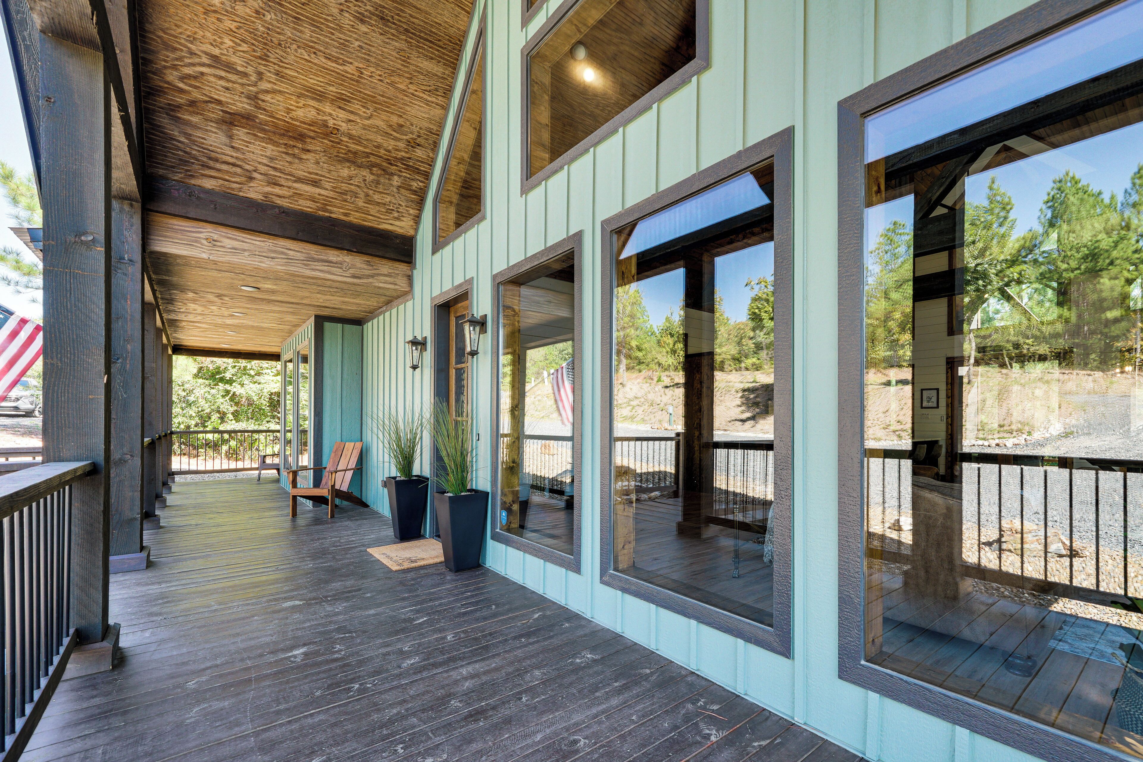 A covered porch with wooden flooring, large windows, and potted plants.