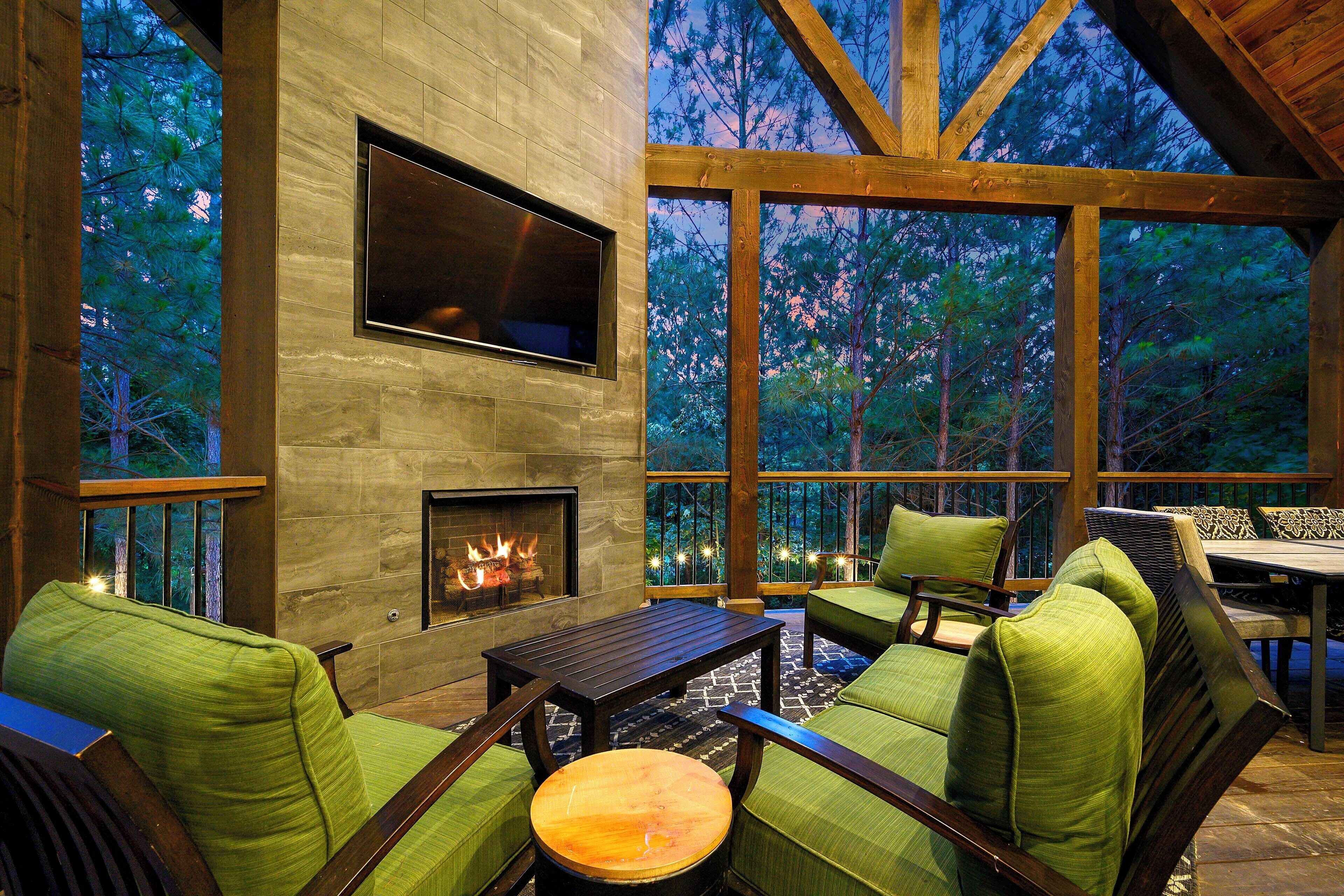 A cozy outdoor seating area with a stone fireplace, green upholstered chairs, and a wooden table.