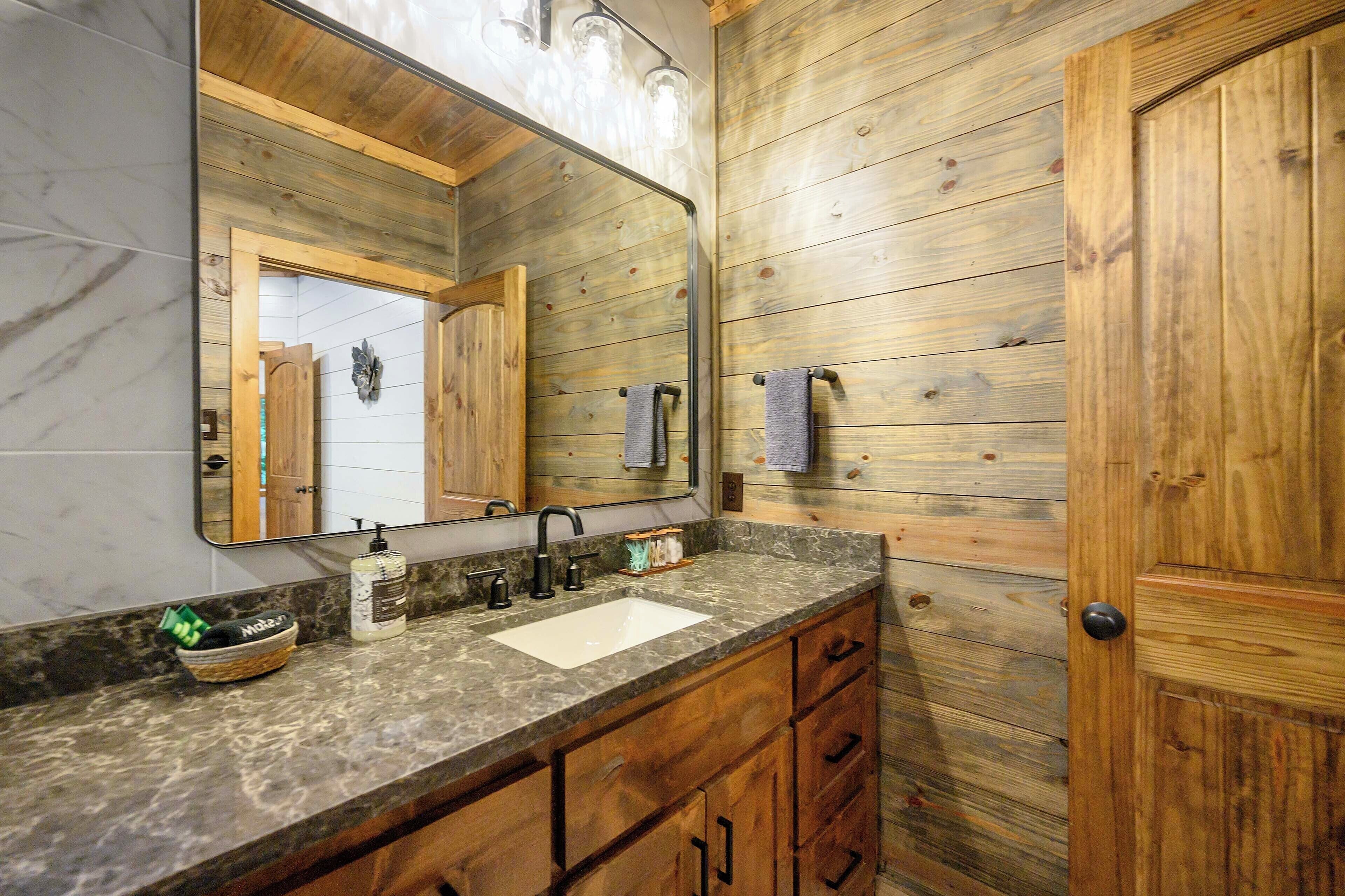 A bathroom with a wooden wall, a marble countertop, a sink, and a large mirror.