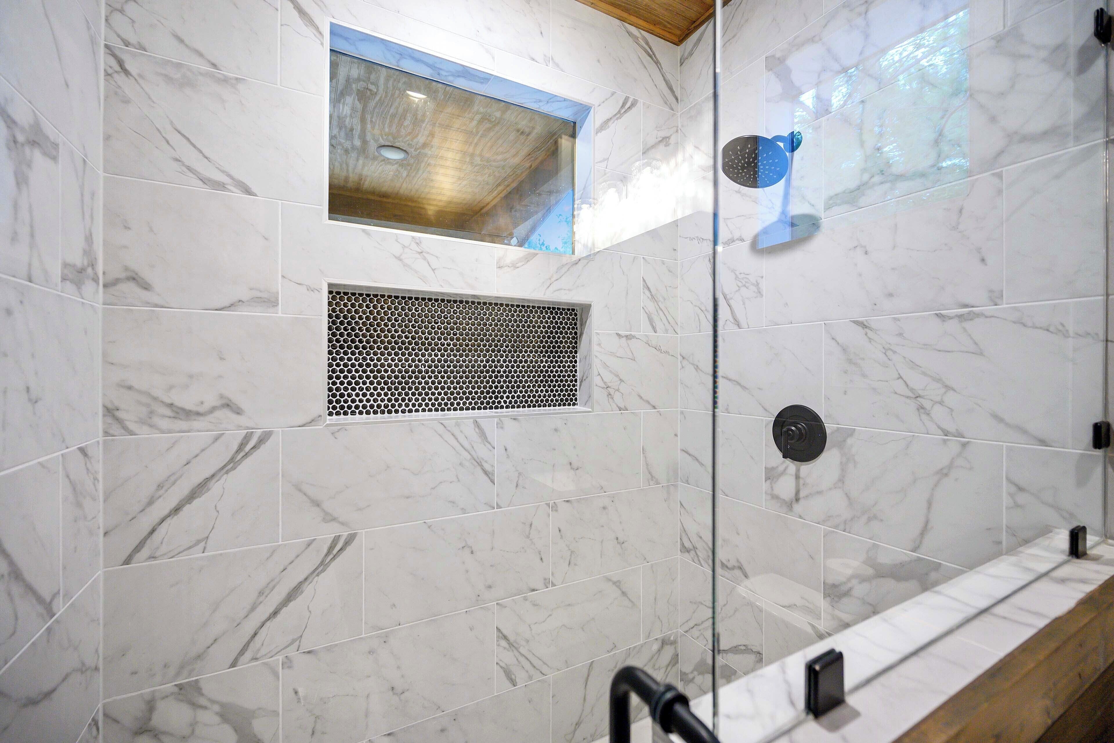 A modern bathroom with marble tiles, a shower with a rain showerhead, a ventilation grille, and a small skylight.