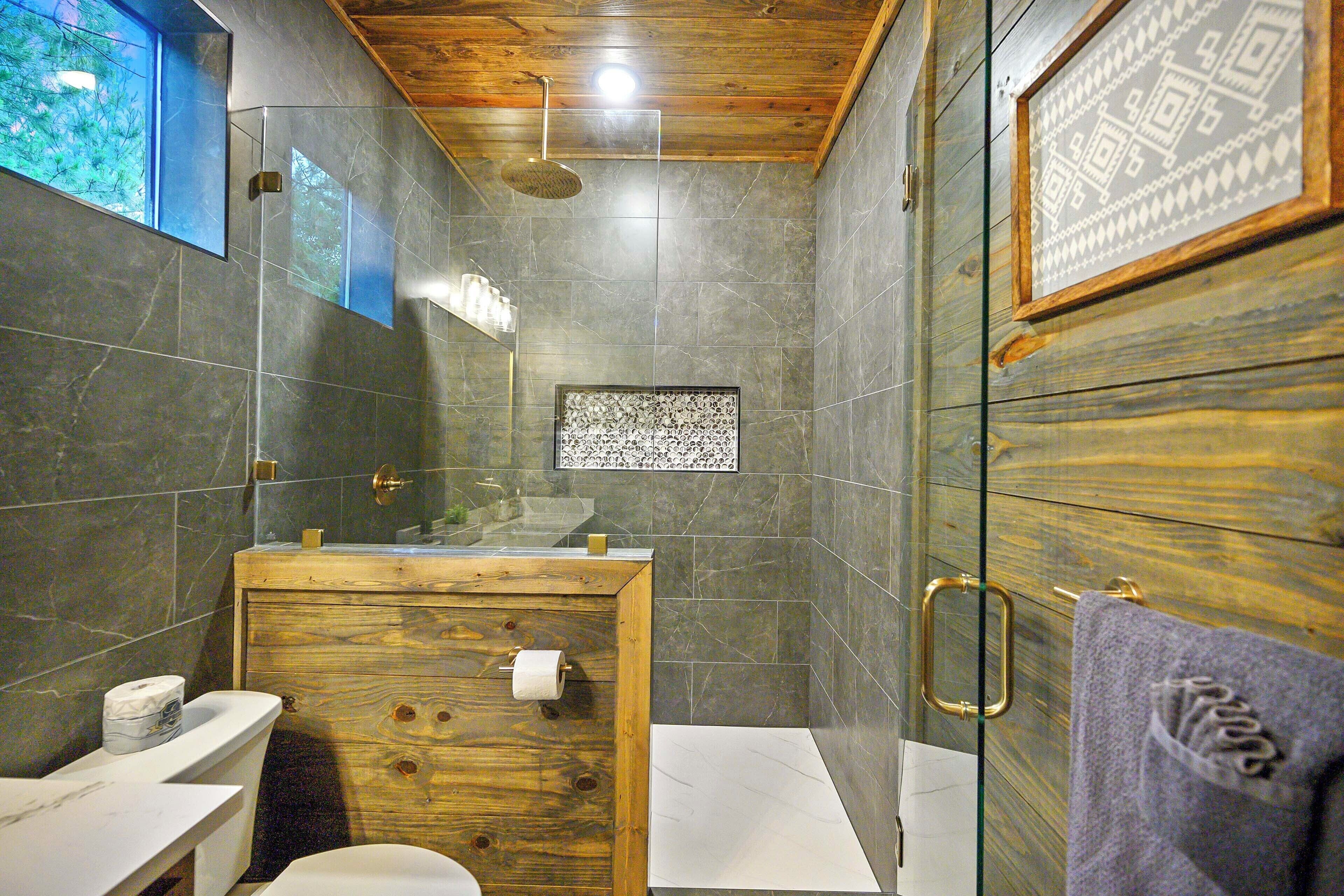 Une salle de bain avec un meuble-lavabo en bois, une cabine de douche en verre et une œuvre d’art encadrée au mur.