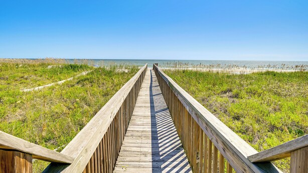A wooden boardwalk leading to a beach with grassy dunes and a clear blue sky. - Private Beach & Pool Access: Murrells Inlet Condo! (Murrells Inlet)
