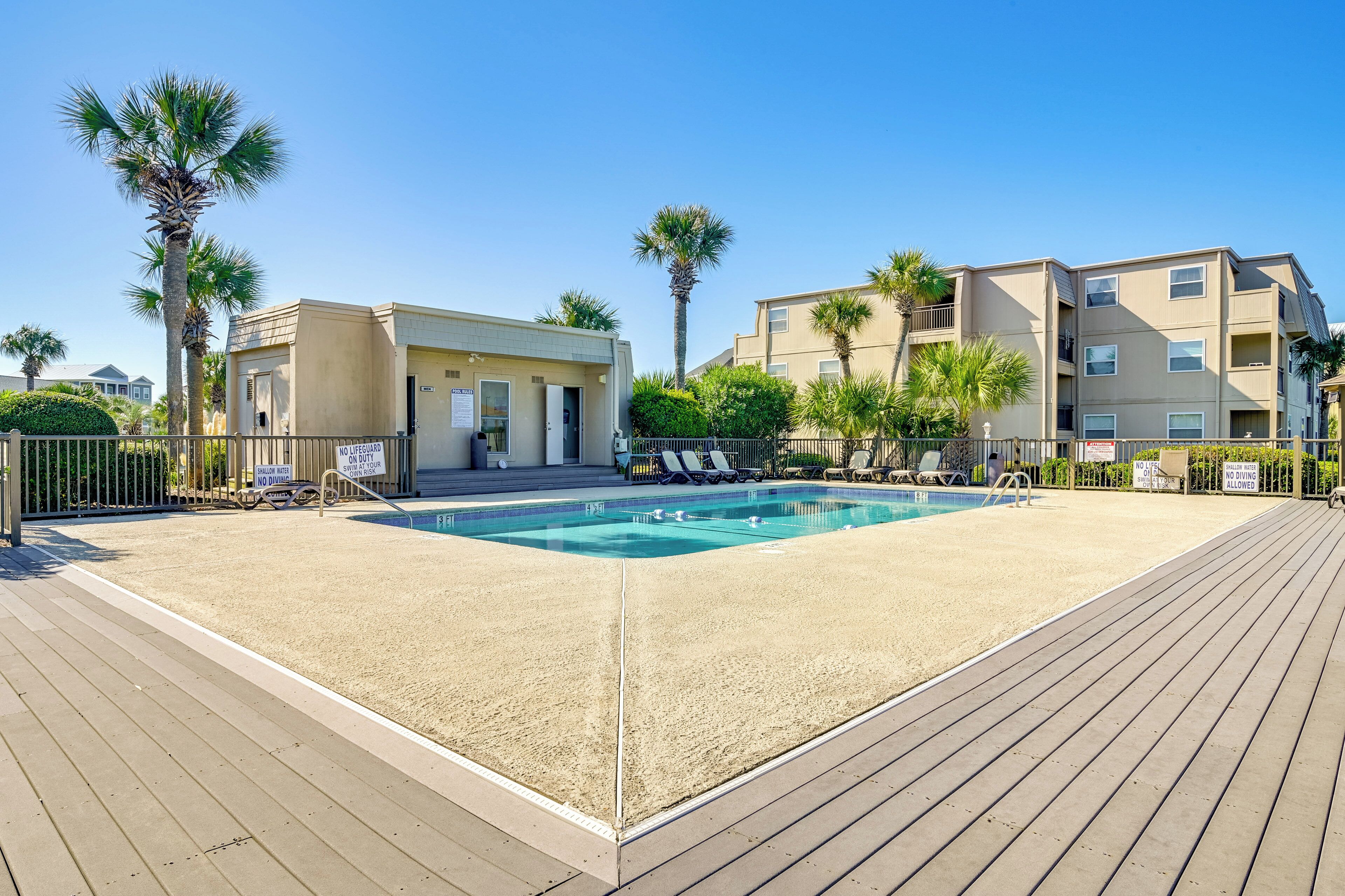 Un espace piscine doté d’une terrasse en bois, de chaises longues et de palmiers.