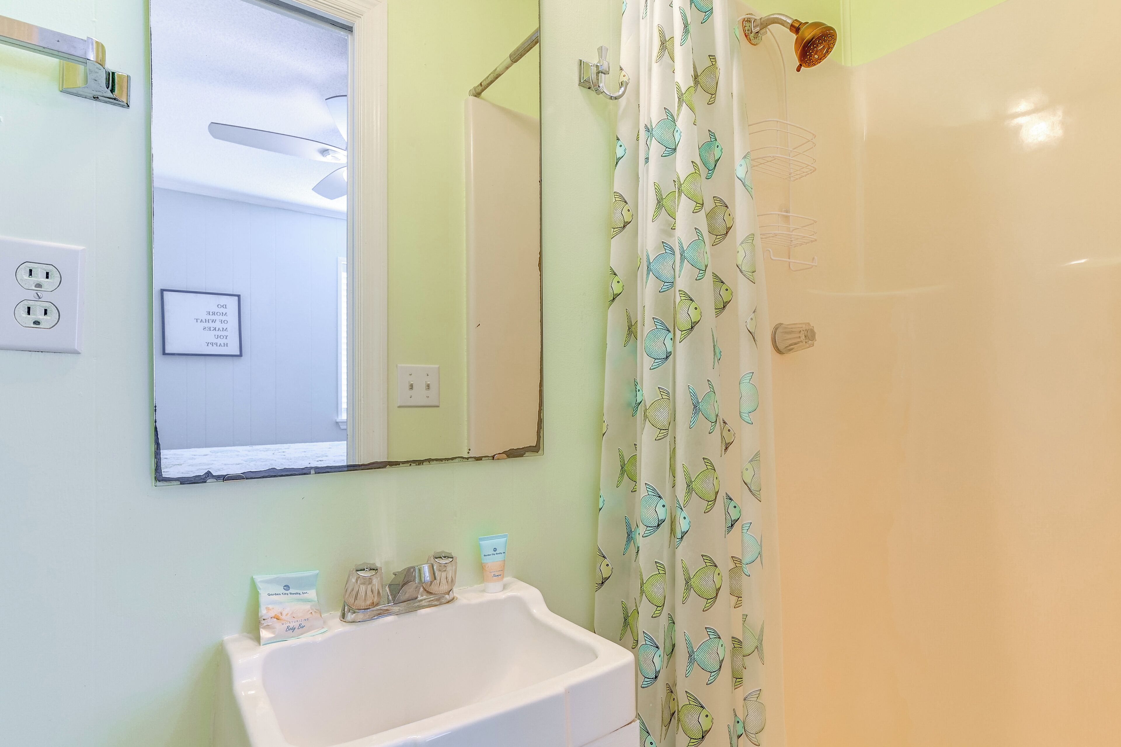 A bathroom with a white sink, a mirror, a shower curtain with fish patterns, and a ceiling fan.